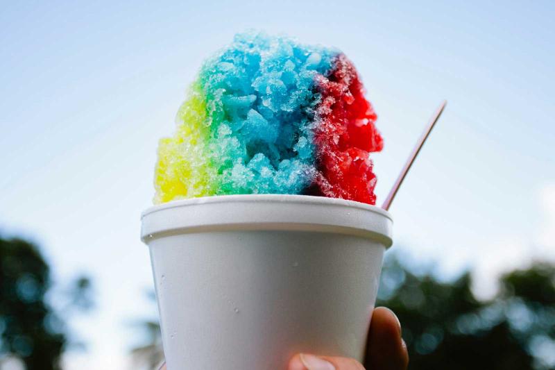 A cup of shaved ice is held up against a blue sky